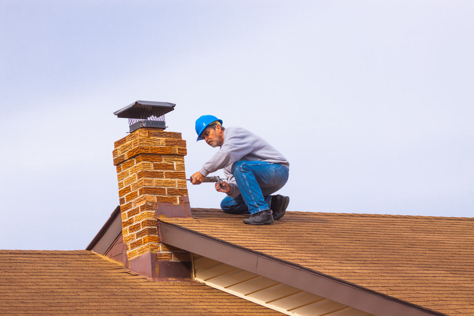 Contractor Builder with blue hardhat on the roof caulking chimney Chimney cap installation in Portsmouth, NH<br />