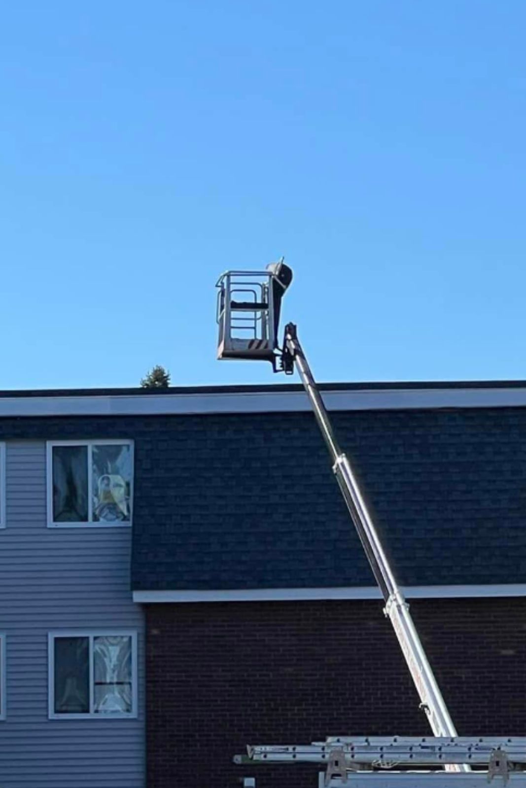Ladder lift elevates worker against blue sky at a building in Sanford, ME, height-focused aerial operation.