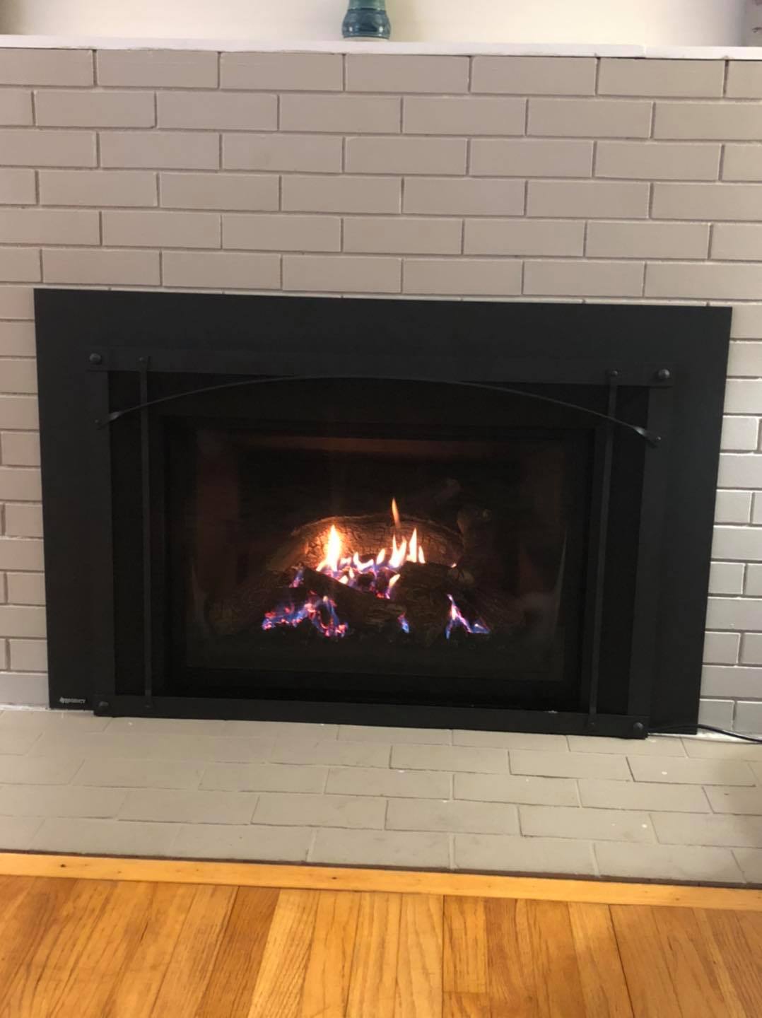 Gas fireplace insert installation in Cape Elizabeth, ME featuring black arched surround and traditional brick fireplace by Frechette Chimney Sweeping.
