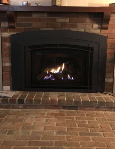Modern gas fireplace insert installed in Westbrook, ME with black steel surround and light gray brick hearth by Frechette Chimney Sweeping.